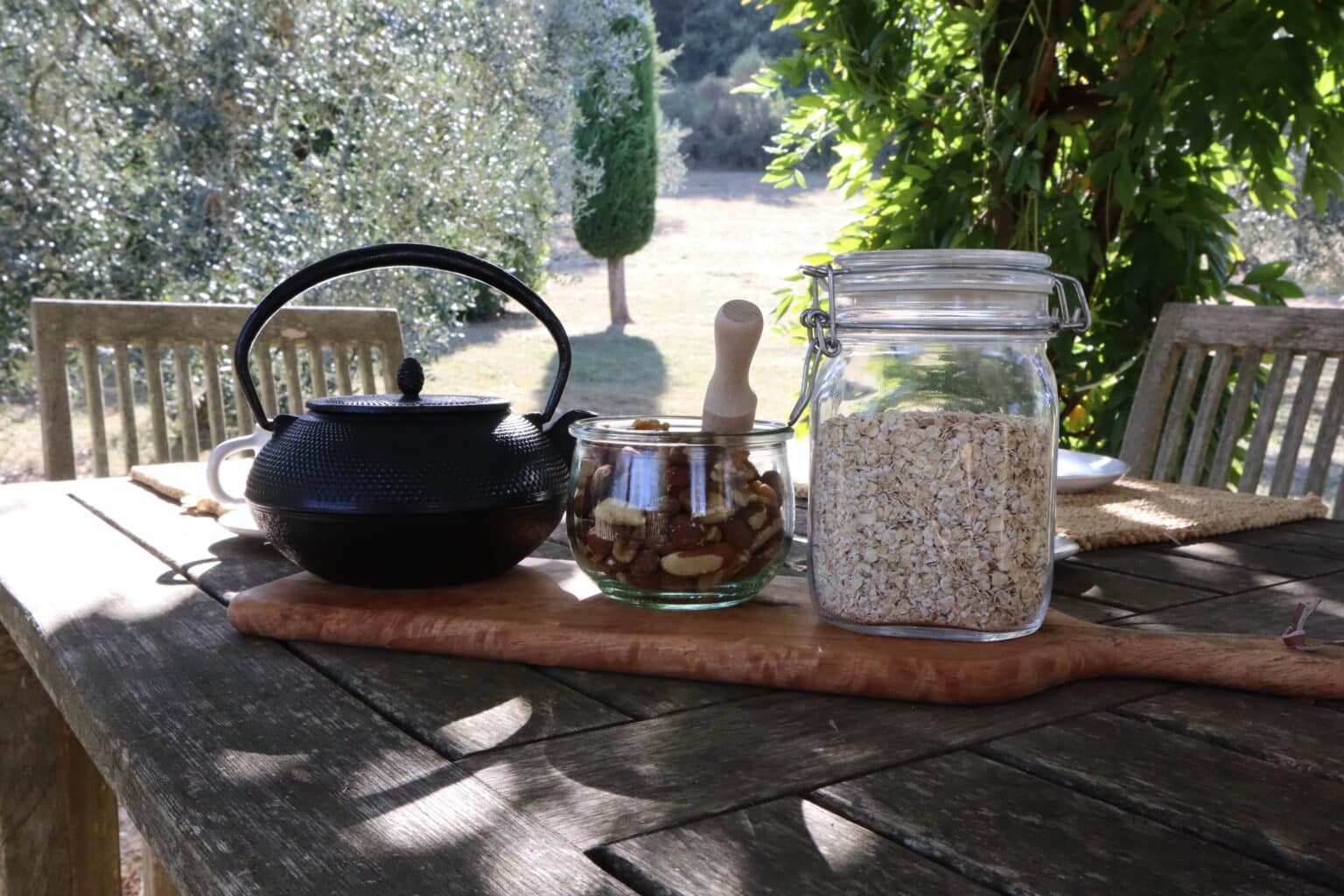 Cast iron teapot, mixed nuts, and oats on a wooden board during an outdoor breakfast at a Val d'Orcia adults-only hotel.