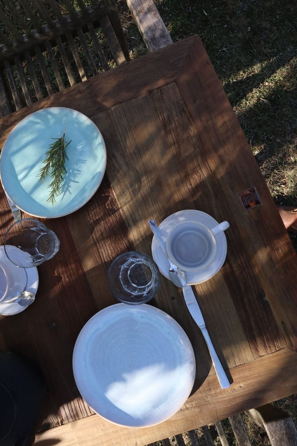 Stilvoll gedeckter Frühstückstisch mit blauen Tellern und Kaffeegeschirr im kühlen Schatten der Bäume auf einem toskanischen Landgut.