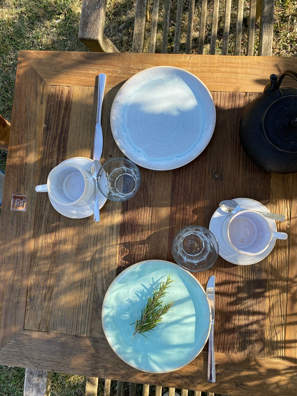 Minimalist rustic table setting with white ceramic plates, rosemary, and coffee cups for a romantic experience couples retreat.