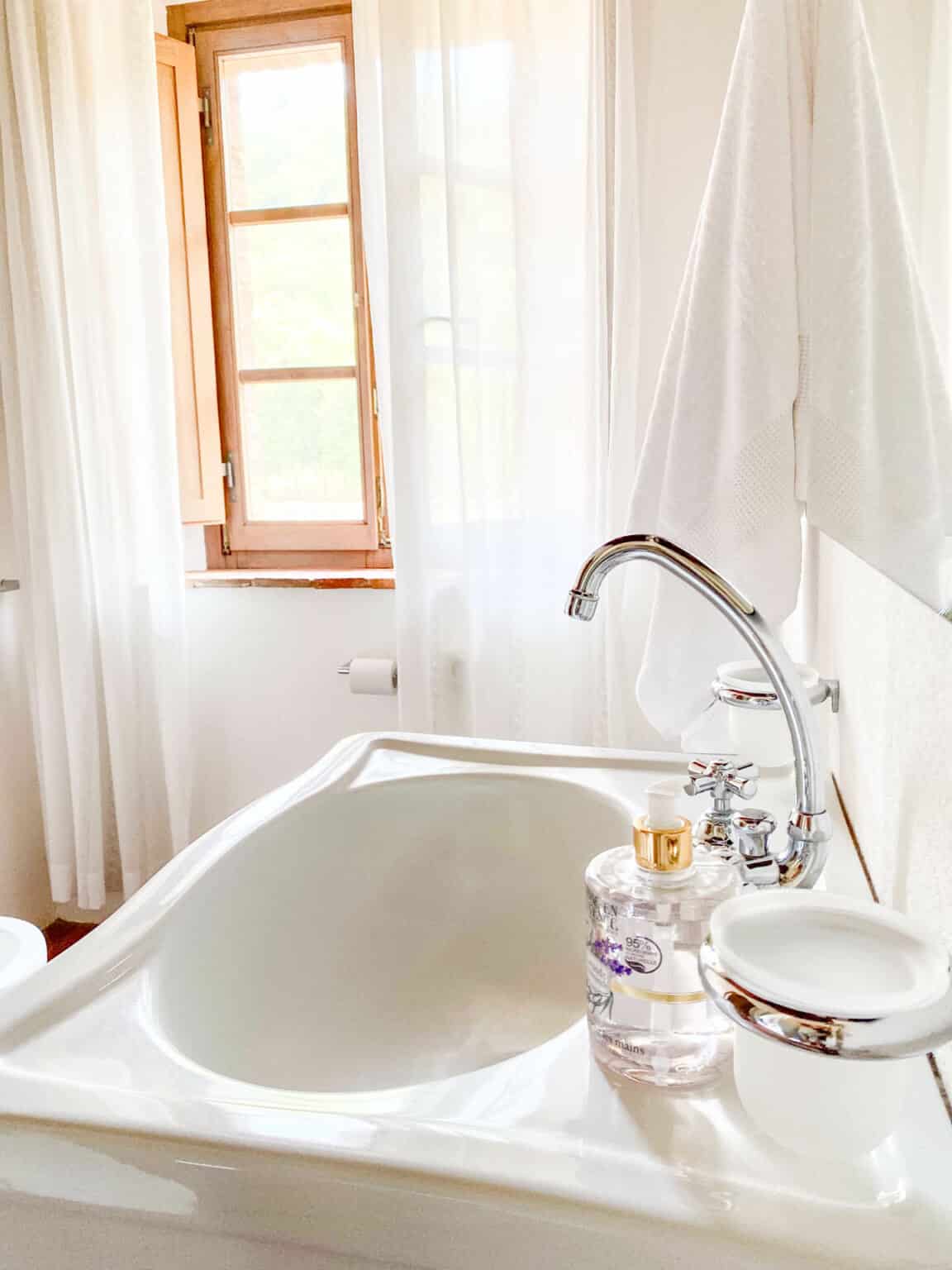 Minimalist luxury bathroom sink with a chrome faucet, clear liquid soap dispenser, and white hand towels at ABBADIA WINE RELAIS.