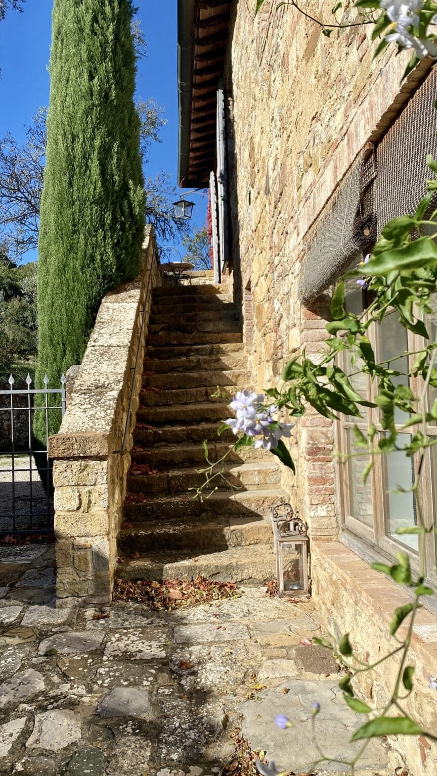 Historic stone staircase and rustic walls alongside a tall cypress tree at ABBADIA WINE RELAIS romantic hideaway.